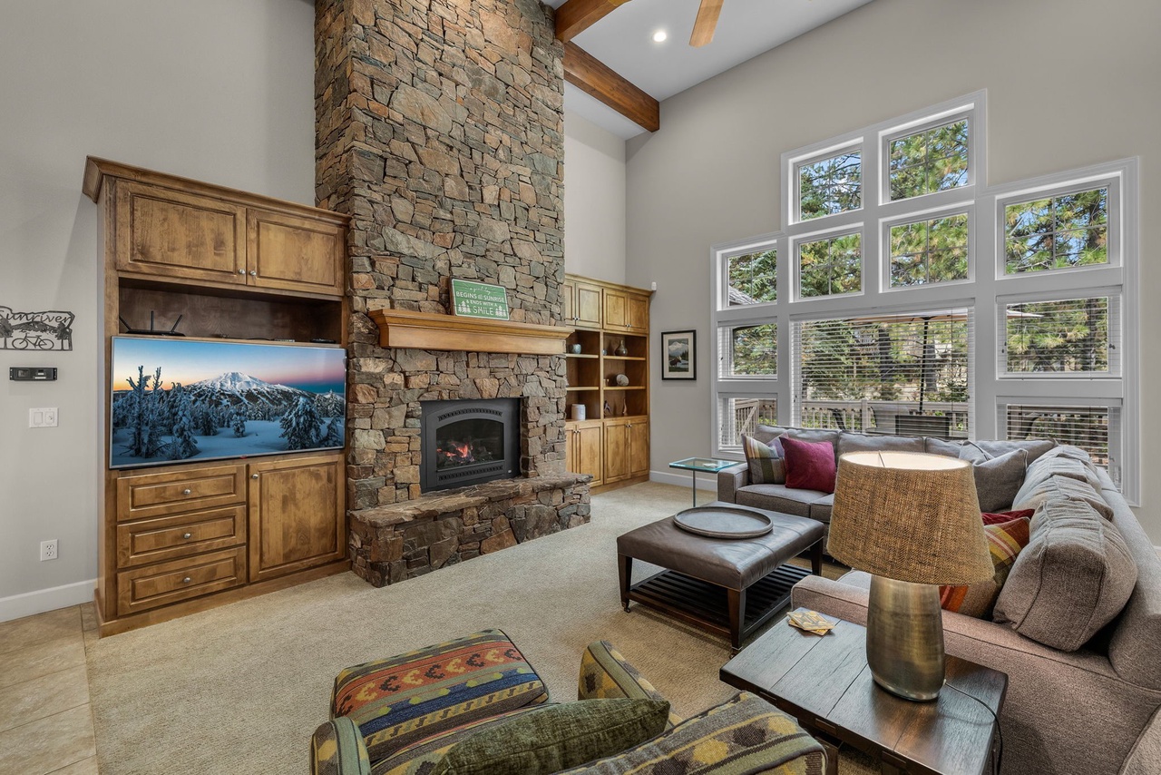 Sink into plush seating in your living room, where a stunning stone fireplace and soaring vaulted ceilings create a warm, inviting atmosphere. Tall windows frame views of towering pines, bringing nature right to your doorstep.