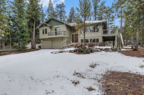 A spacious mountain retreat nestled among towering pines, featuring winter charm with snow-dusted landscaping and forest surroundings.