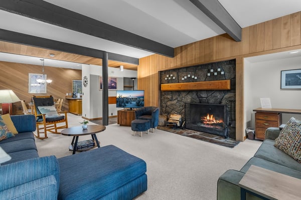 Gather in this warm living room where exposed beams meet modern comfort. The stone fireplace crackles invitingly while plush seating awaits.