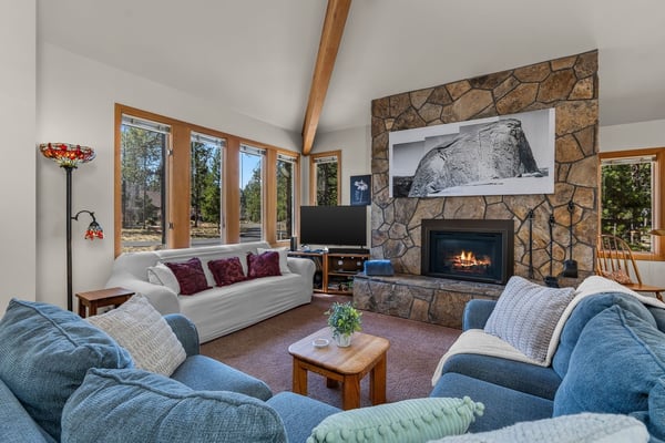 Sink into plush seating by your crackling stone fireplace as natural light floods this inviting living space through panoramic windows.