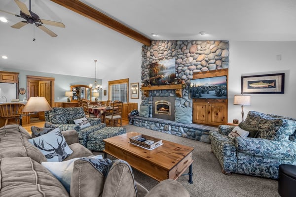 Gather around the stone fireplace in this warm living room, where rustic wood accents and plush seating invite you to relax after a day of adventure.