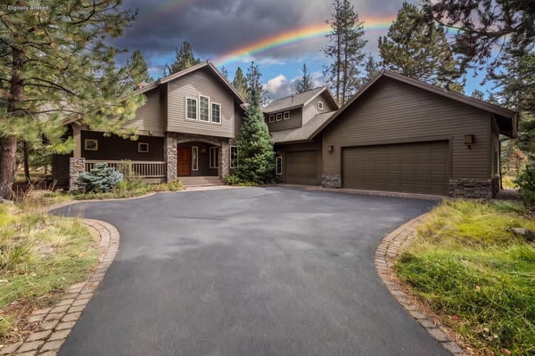 A welcoming mountain property surrounded by towering pines, featuring stone and wood accents under a dramatic rainbow sky.