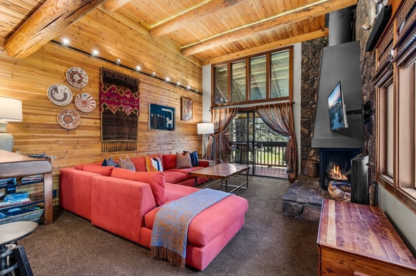 Curl up on plush seating by a crackling fireplace under soaring wood-beam ceilings, with natural light pouring through large windows offering views of the surrounding landscape.