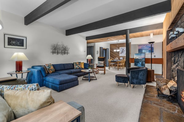 Relax in your spacious living room with exposed beams, cozy fireplace, and rich blue sectional perfect for unwinding after mountain adventures.