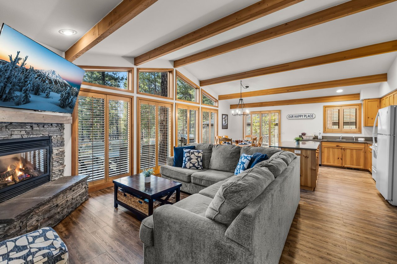 Cozy up in your open-concept haven with soaring beamed ceilings, crackling fireplace, and forest views through floor-to-ceiling windows.