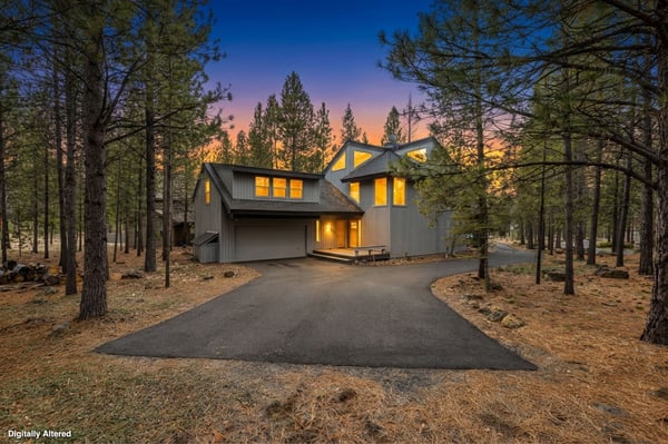 Modern mountain retreat nestled among towering pines with warm interior lighting creating a welcoming glow at twilight.