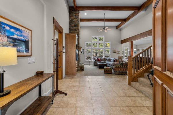 Step into your welcoming mountain escape with soaring ceilings, warm wood beams, and a cozy stone fireplace anchoring the open living room beyond.