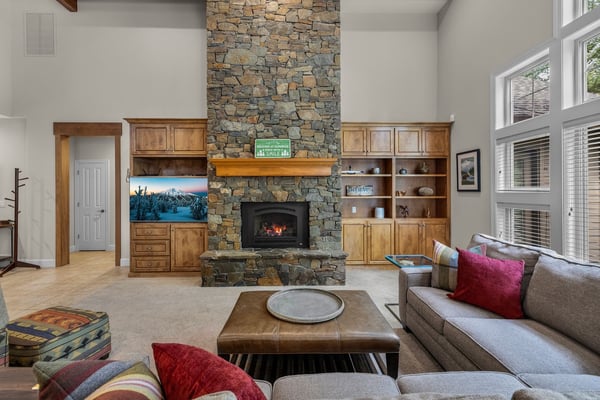 Gather around the glowing fireplace framed by stunning stonework and warm wood built-ins, where soaring ceilings and soft natural light create your perfect retreat.