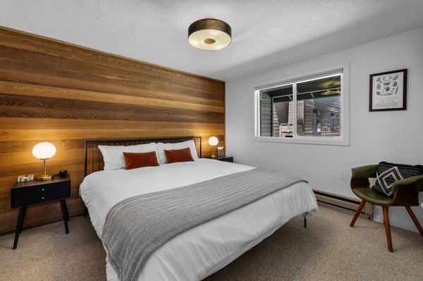 Sink into crisp white linens and soft textures in your inviting bedroom. The warm wood accent wall and thoughtful lighting create the perfect space for restful nights after your mountain adventures.