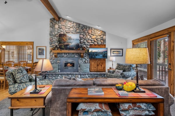Unwind in your inviting living space with vaulted ceilings, a stunning river rock fireplace, and warm natural light streaming through large windows.