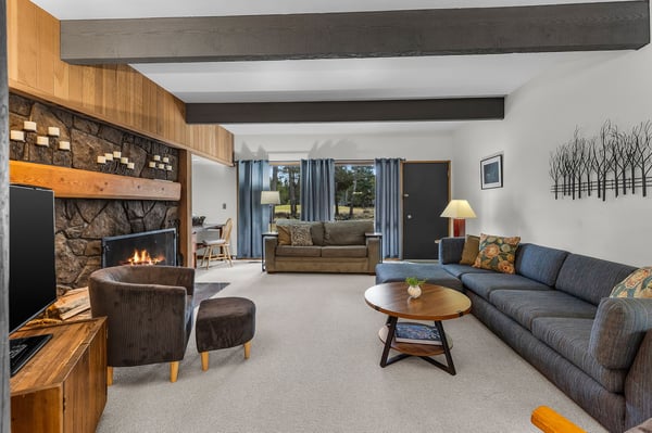 Gather around the crackling stone fireplace in your spacious living room, where modern comfort meets rustic charm with exposed beams overhead.